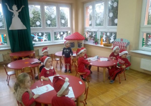 dzieci z grupy II w czerwonych czapkach siedzą przy stolikach